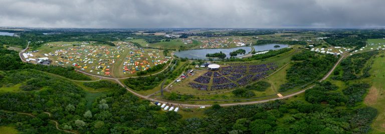 Luftfoto af Spejdernes Lejr 2026 i Hedeland med teltby, sø og den store lejrbålsscene